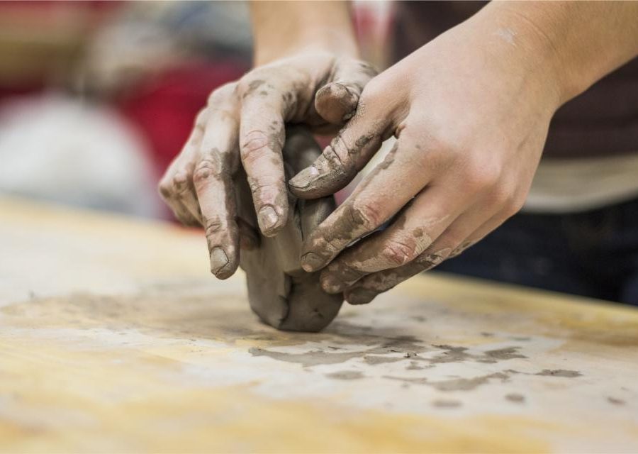 Small hands pressing and shaping a lump of clay on a wooden table