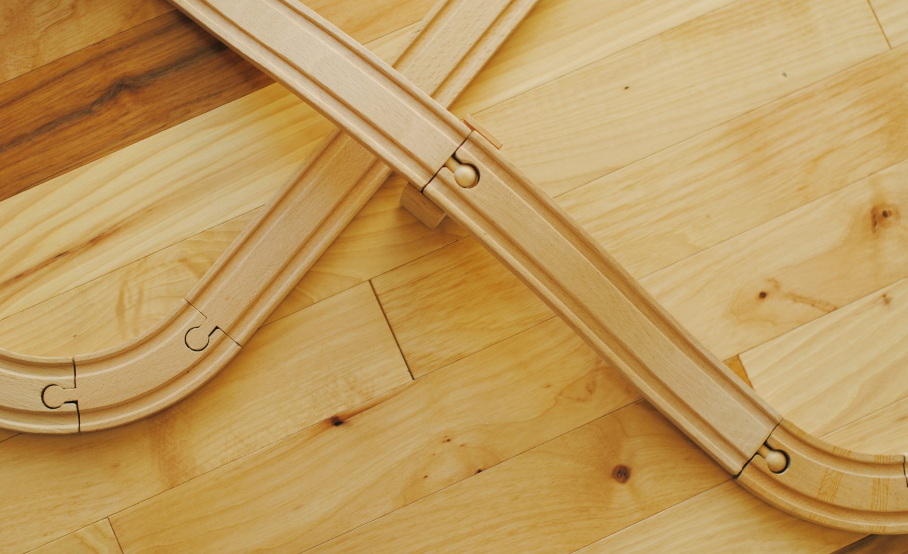 Wooden train track curving across a pale wooden floor