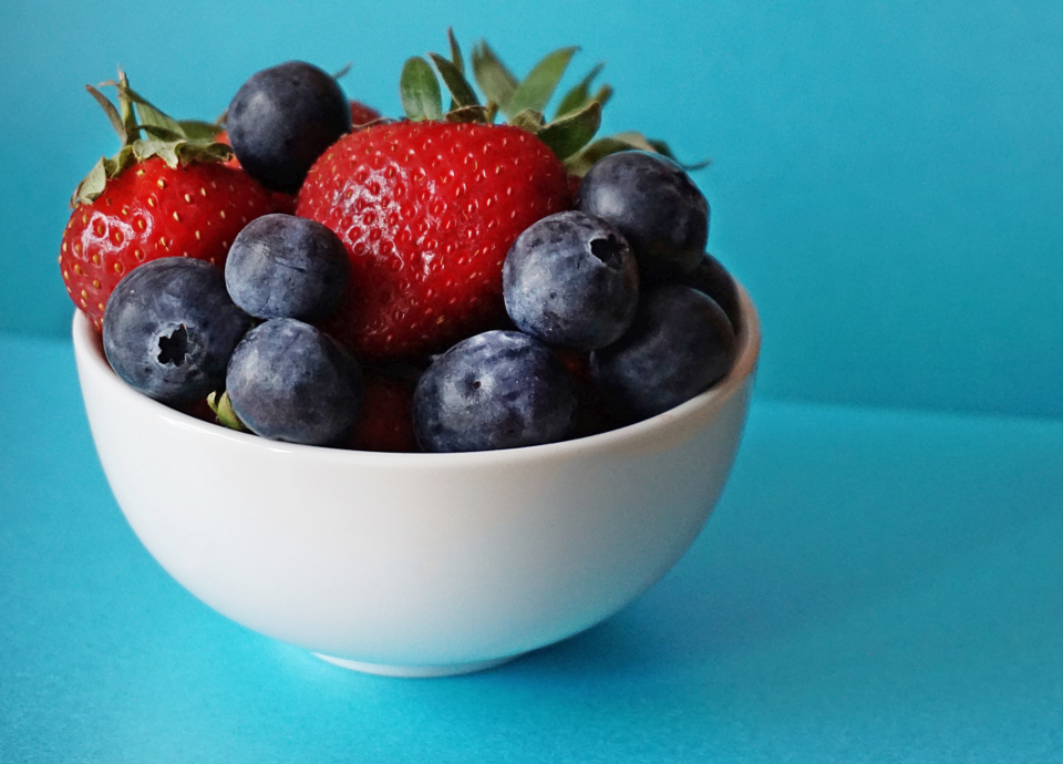 A white bowl of strawberries and blueberries on a bright teal table