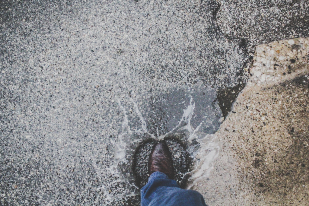 A boot splashing into a puddle on wet ground